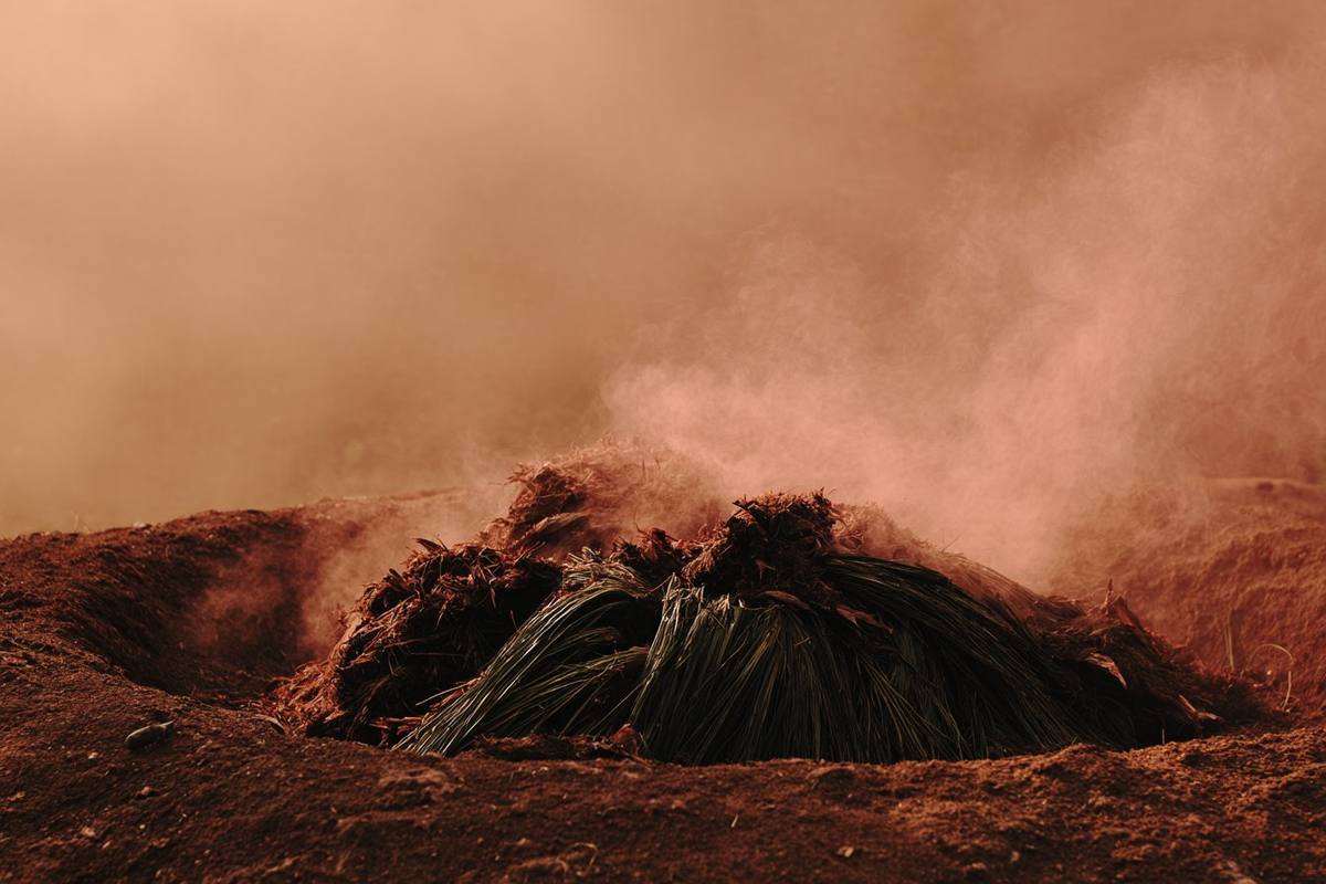 An earthen pit oven with smoke rising